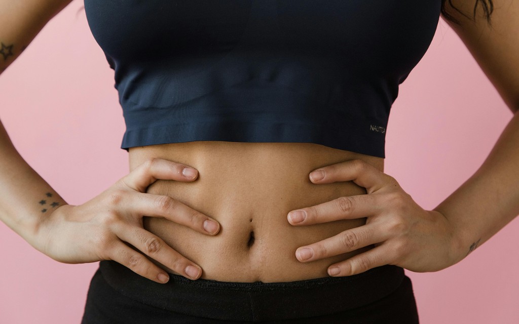 Person in athletic wear with hands resting on their midsection against a soft pink background
