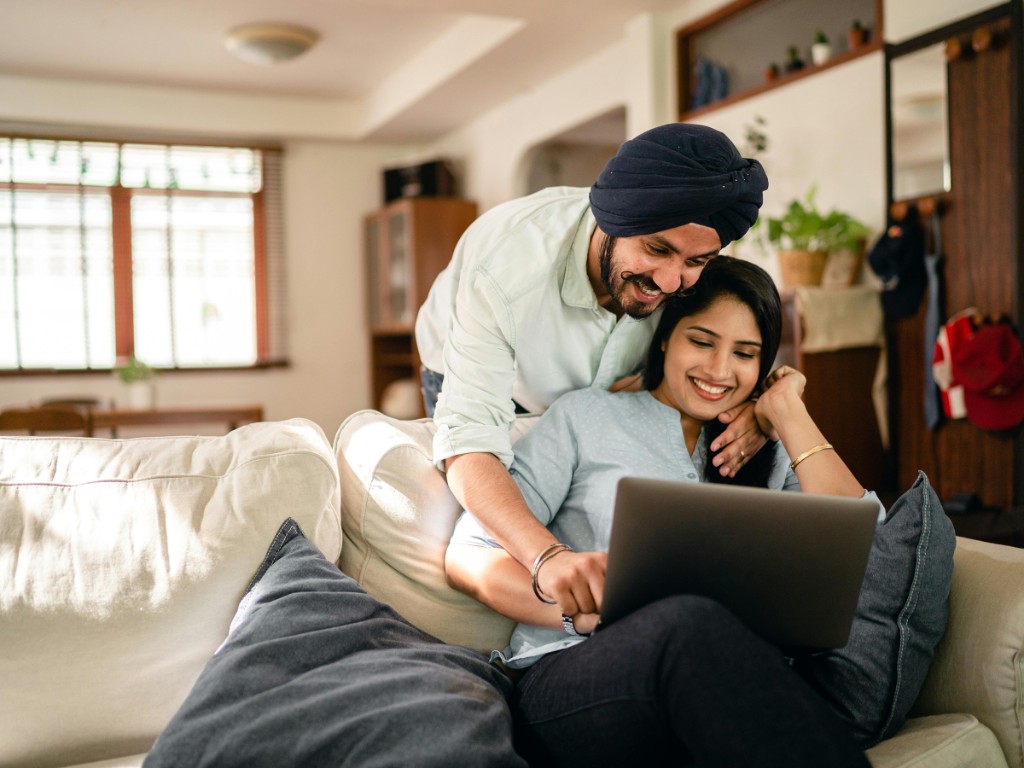 Couple at home on a sofa, smiling while looking at a laptop together